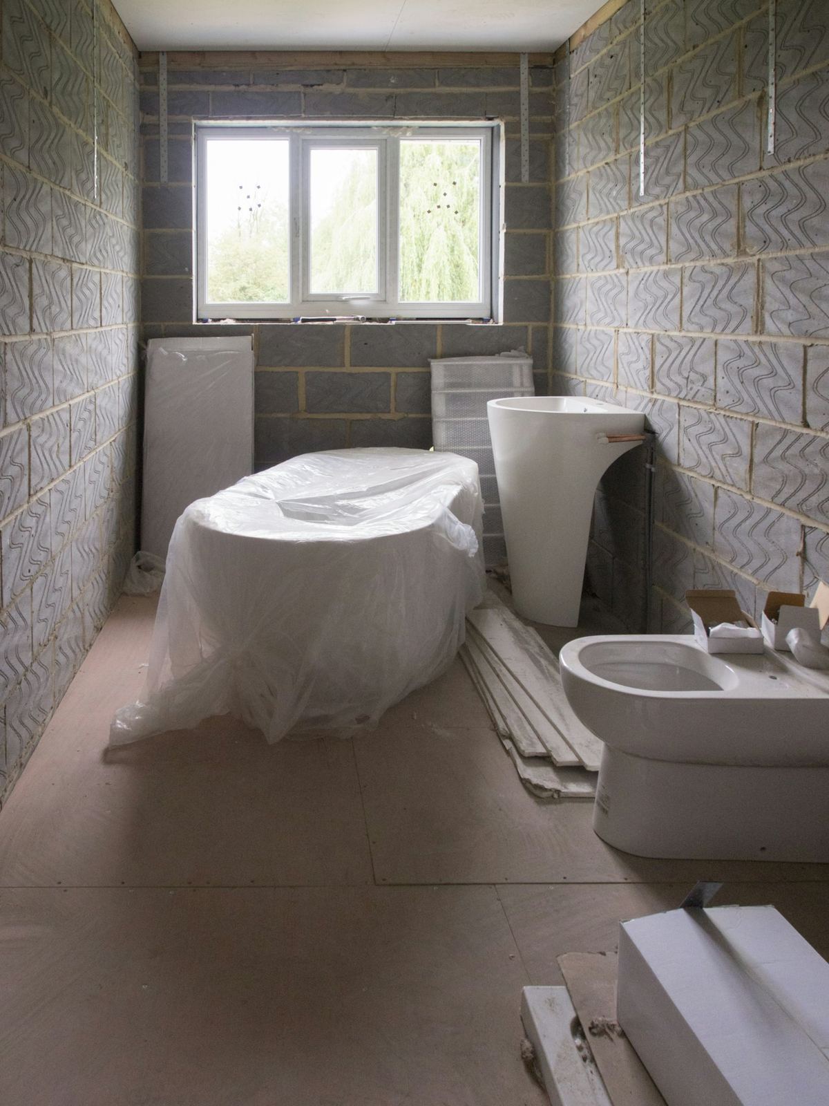 A bathroom mid-refit, blockwork walls, sanitaryware wrapped on the floor